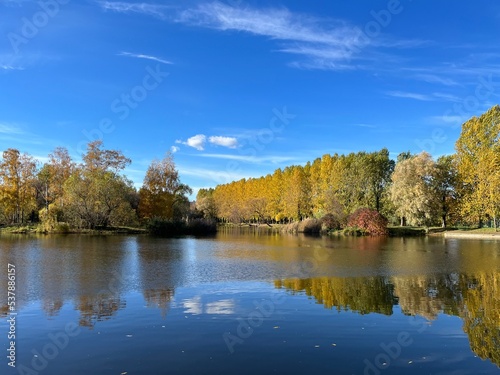 Autumn trees silhouettes reflection on the surface of the lake, blue sky