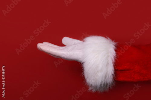 Santa Claus hand presenting your text, product, advertisement on a red background.Mockup. Copy space.