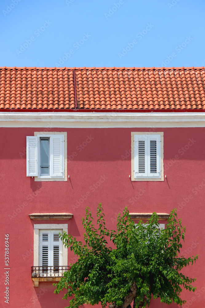 Traditional mediterranean building with pink facade and white windows. Traditional architecture in Supetar, island Brac, Croatia.