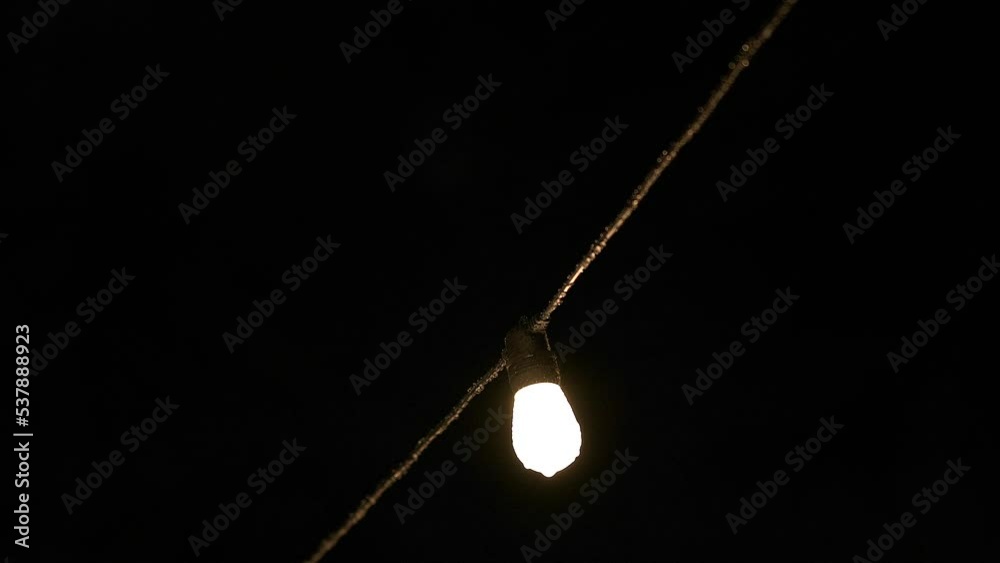 Single string light with rain splashing off it and the wire against black sky