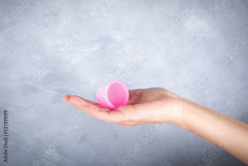 Close-up of woman's hand holding the menstrual cup over grey background.