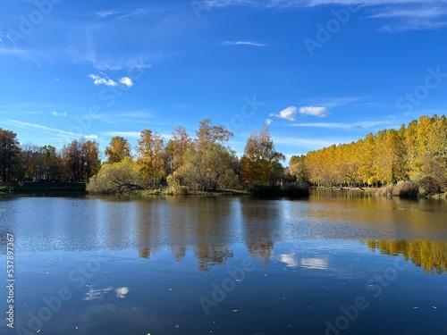 Autumn trees silhouettes reflection on the surface of the lake, blue sky