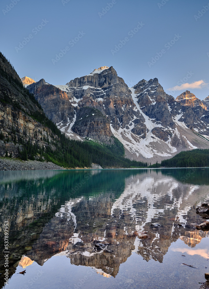 Obraz premium The mountain peaks of the Three Sisters reflected in the calm evening waters of Moraine Lake Canada