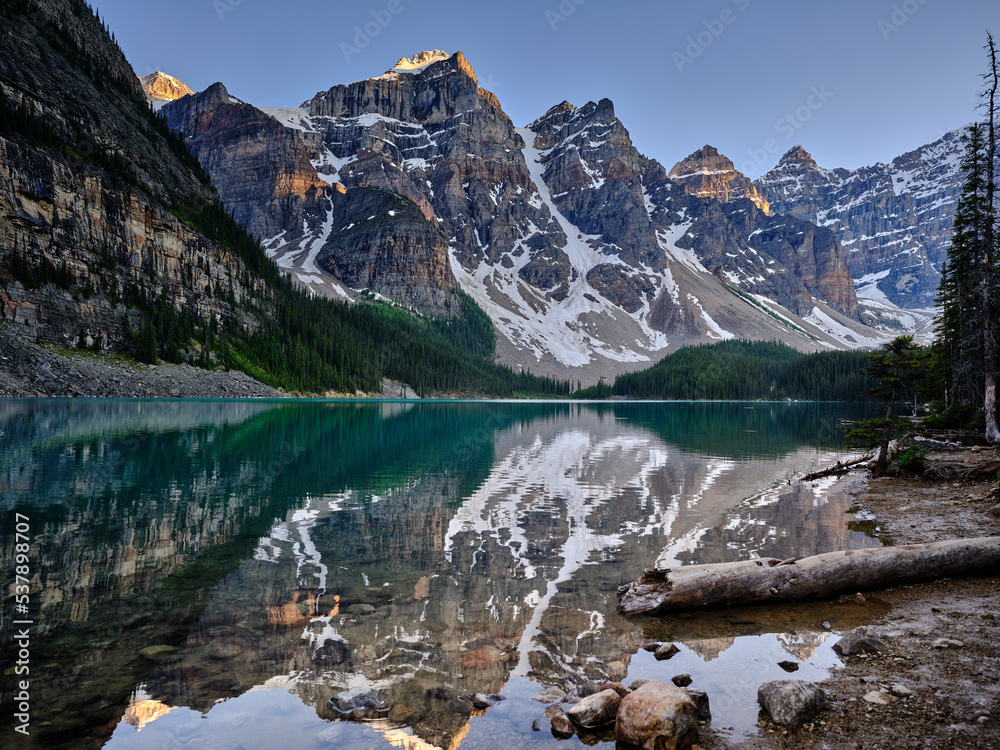 The mountain peaks of the Three Sisters reflected in the calm evening waters of Moraine Lake Canada