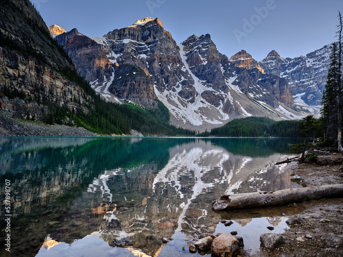 The mountain peaks of the Three Sisters reflected in the calm evening waters of Moraine Lake Canada