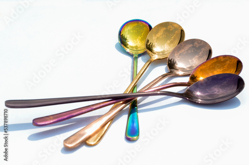 Multicolored table spoons on a plain white background, picture for an article about tableware or cutlery, with copyspace