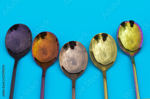 Multicolored table spoons on a plain blue background, picture for an article about tableware or cutlery, with copyspace