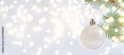 Mockup white christmas ball on a fir tree branch with festive bokeh on a light background. Wide horizontal banner with copy space. Winter and christmas concept