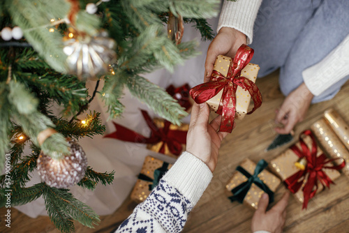 Family exchanging christmas gifts under christmas tree in festive decorated room close up. Merry Christmas and Happy Holidays! Couple hands exchanging with wrapped presents top view