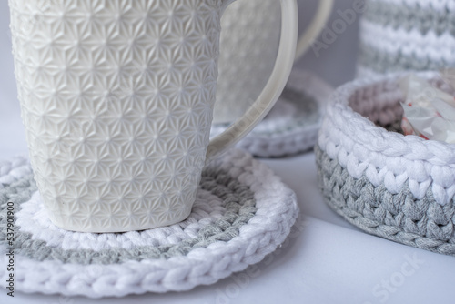 striped white with gray coaster, white winter coffee mug and basket with sweets, striped crochet basket, nature-friendly sustainable handicraft business, cute interior items. Space for your text