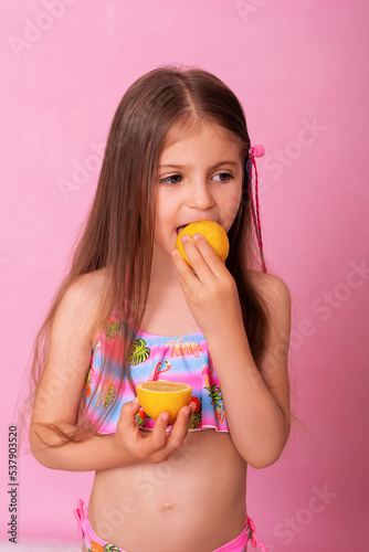 Caucasian beautiful little girl with fresh yellow lemons on a pink background. Little girl with lemon. Funny child isolated on pink.