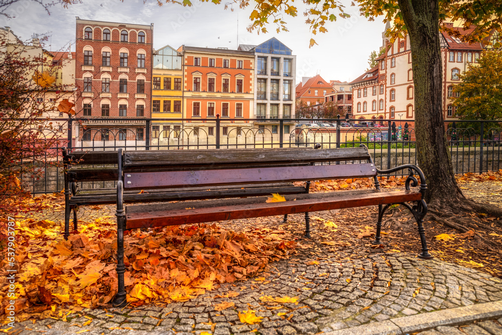 jesienne ławka z kolorowymi liśćmi przy ulicy z kolorowymi domami w Opolu (Polska) - obrazy, fototapety, plakaty 