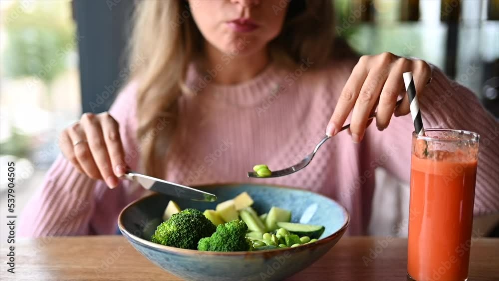 Woman eating a green salad with broccoli, apple, avocado, beans, soia and olive oil