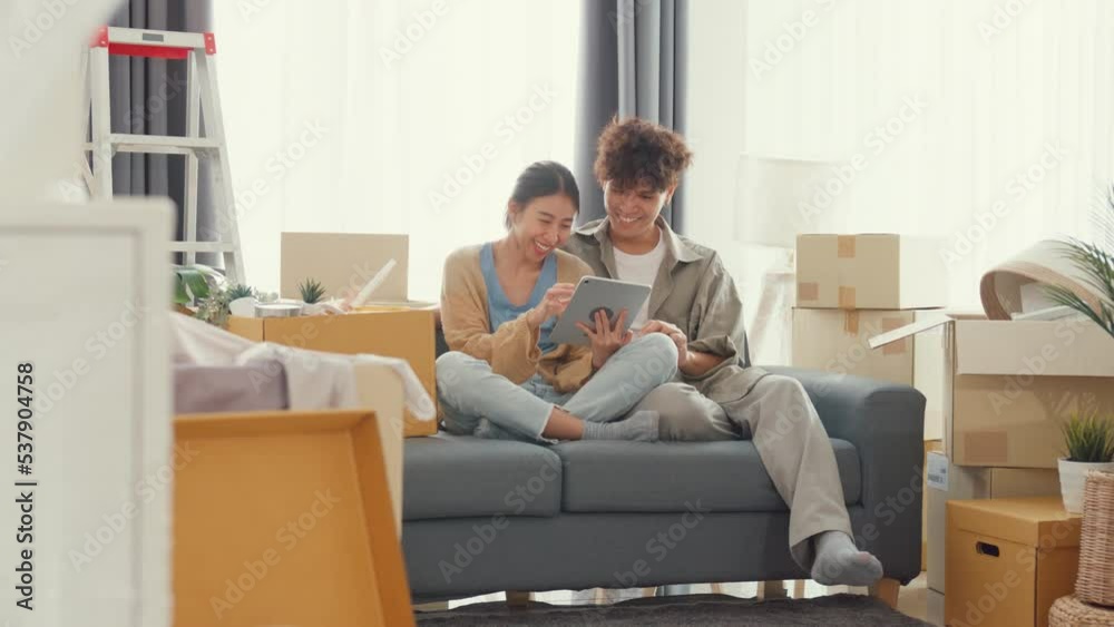 Young happy Asia couple sit on sofa couch use digital tablet online shopping furniture from decoration store in living room at home. Husband wife move new house, Apartment Rent And Ownership Concept.