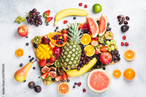 Fototapeta Naklejka Na Ścianę i Meble -  Healthy raw rainbow fruit platter mango papaya strawberries oranges blueberries pineapple watermelon on wooden board on white concrete background, top view, selective focus
