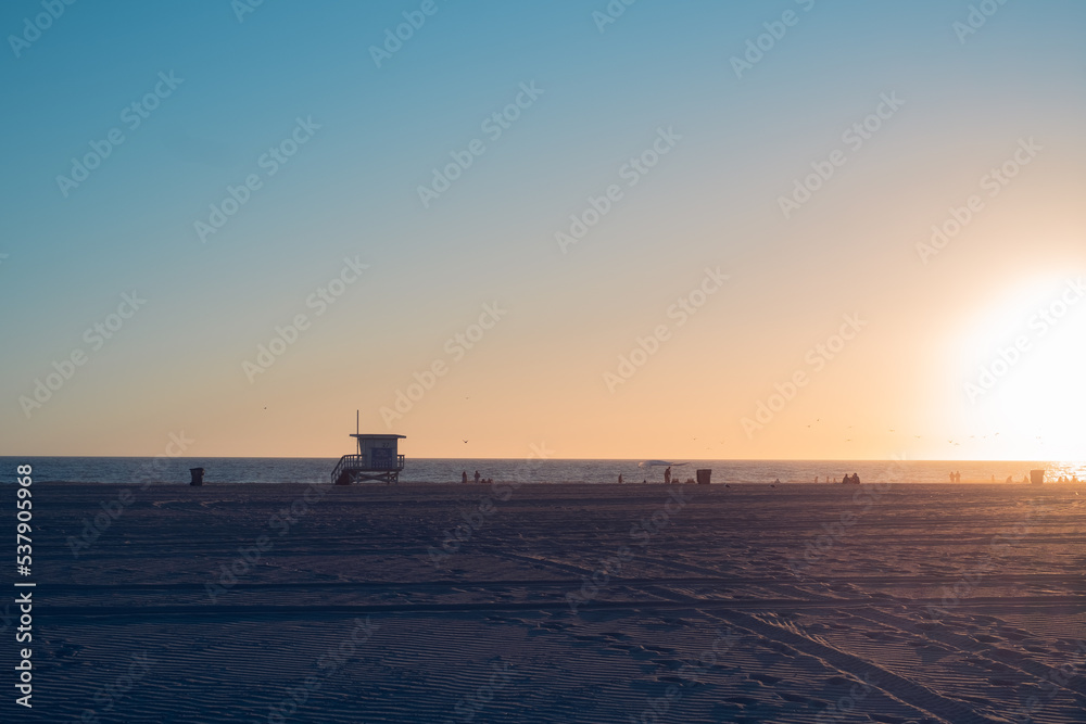 Baywatch tower on the beach during sunset with people strolling by