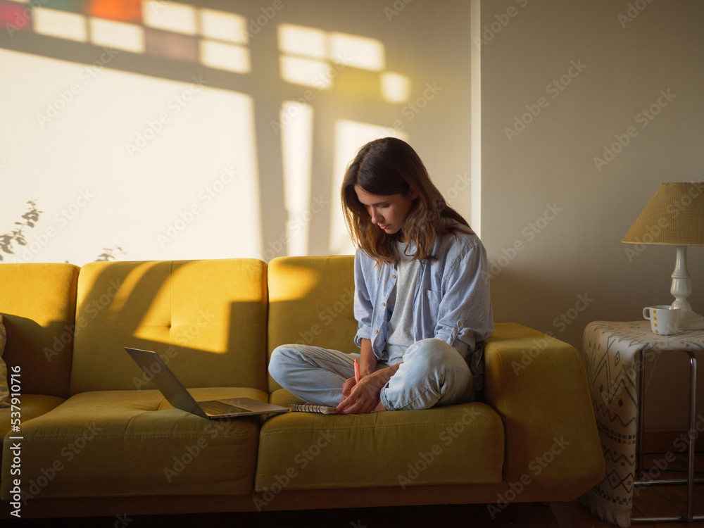 Woman with laptop and notebook sitting on the sofa at home Woman with laptop and notebook sitting on the sofa at home