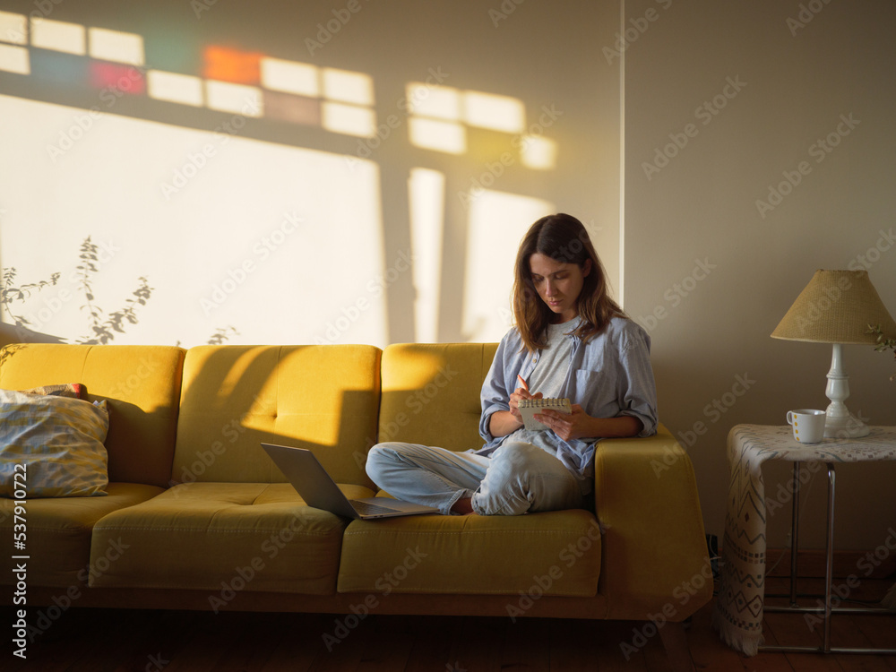 Woman with laptop and notebook sitting on the sofa at home Woman with laptop and notebook sitting on the sofa at home