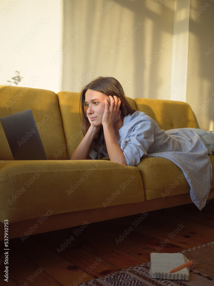 Woman with laptop and notebook laying on the sofa at home Woman with laptop and notebook laying on the sofa at home