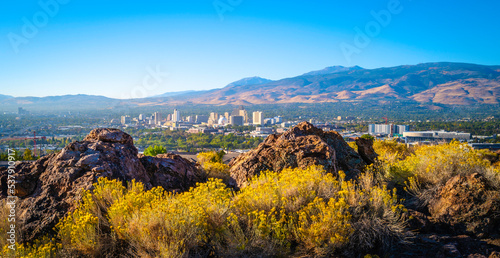 Reno autumn city skyline over Nuttall’s Rayless-Goldenrod flowers and red rock hill in the state capital of Nevada, aerial view of the arid landscape of the desert city photo