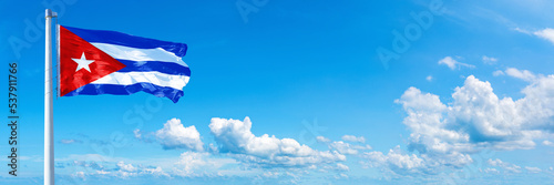 Cuba flag waving on a blue sky in beautiful clouds - Horizontal banner