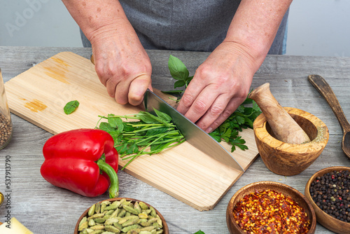 Woman cutting parsley and basil with a knife on a wooden board