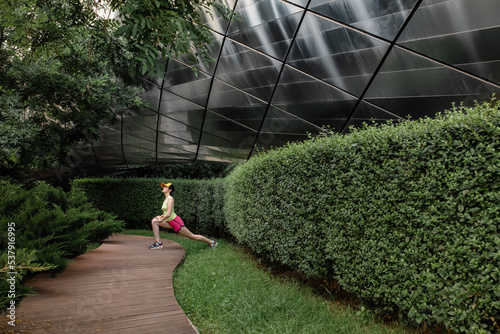 A slender girl is doing fitness near a modern facade and greenery photo