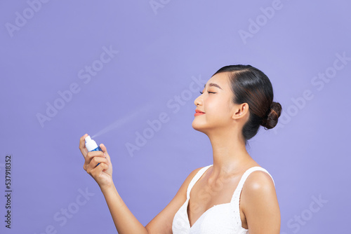 Beautiful woman applying spray water treatment on face