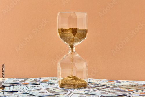 Close up of hourglass placed on bunch of dollars.