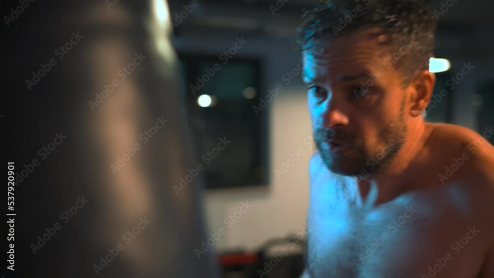Alone boxer is working out blows on a punching bag in a gym in evening Alone boxer is working out blows on a punching bag in a gym in evening