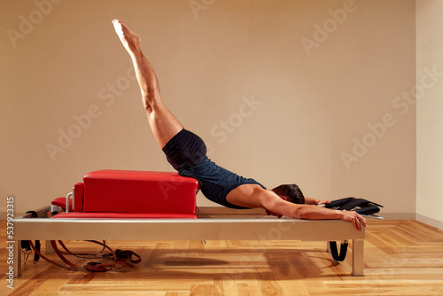 Handsome pilates male instructor performing stretching balance fitness exercise on small barrel equipment, at the pilates studio modern onterior indoor. photo