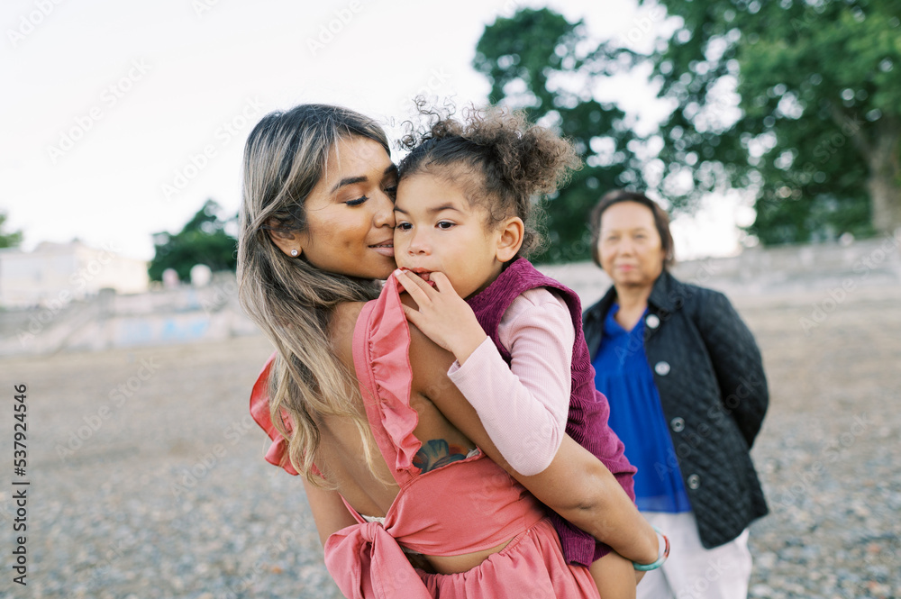 Mother and daughter hugging at the beach with the grandma nearby Mother and daughter hugging at the beach with the grandma nearby