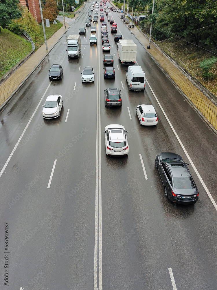 A variety of cars drive on an asphalt two-way road in perspective in the city