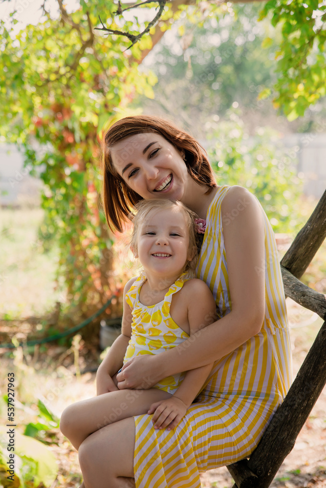 Fototapeta premium Mother and daughter embrace in the park. Woman and little girl spend time together outdoor. Mom and her child. Family concept