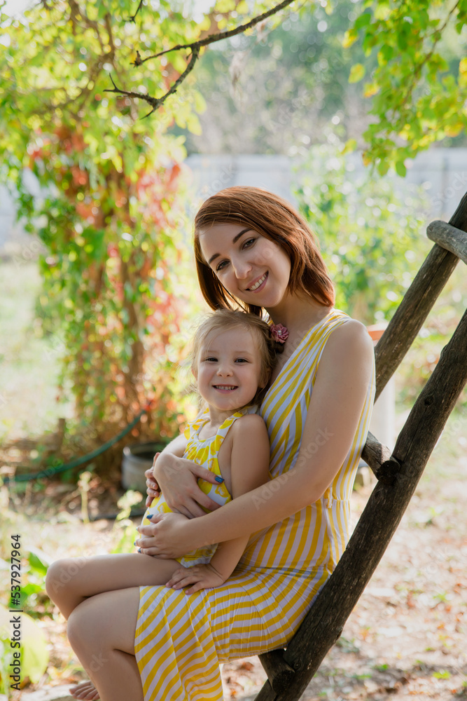 Fototapeta premium Mother and daughter embrace in the park. Woman and little girl spend time together outdoor. Mom and her child. Family concept