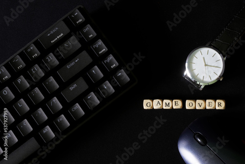 Inscription Game over on black background next to wristwatch, mechanical gaming keyboard and computer mouse. Gambling and the predetermination of the finale. Deadline and defeat. Game over.