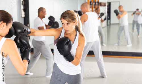 Young concentrated woman practicing boxing punches in sparring during group self defence course in gym © JackF