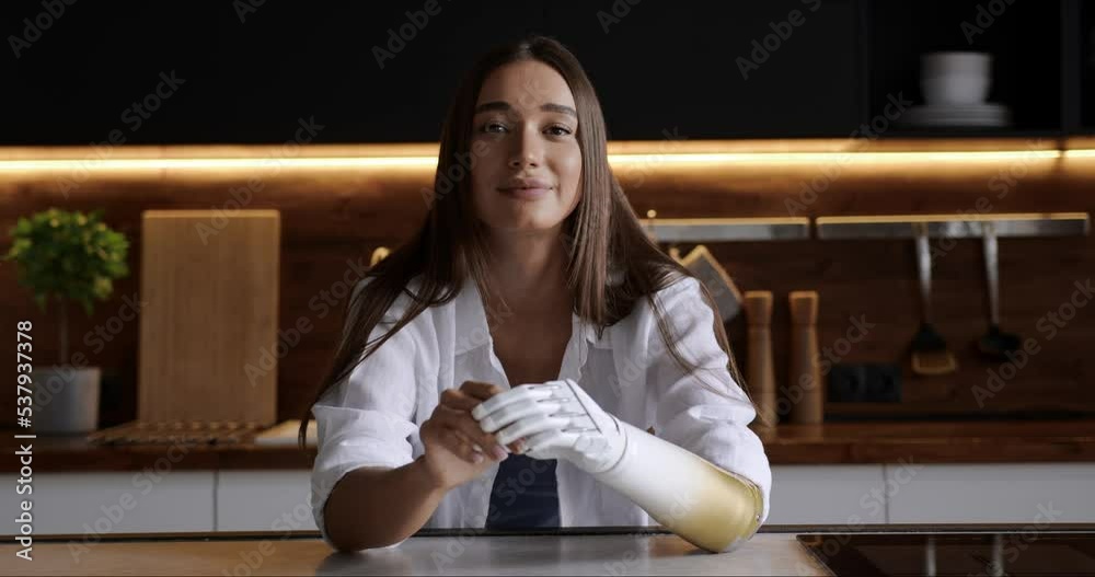 Portrait smiling happy woman with prosthetic arm relaxing on kitchen at home, girl with disability artificial prosthetic limb Portrait smiling happy woman with prosthetic arm relaxing on kitchen at home, girl with disability artificial prosthetic limb