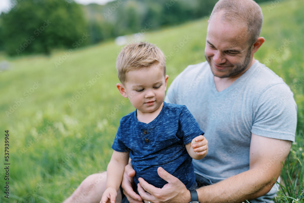 smiling father and son in grass together smiling father and son in grass together