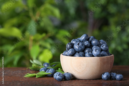 Tasty fresh blueberries and green leaves on wooden table outdoors, space for text