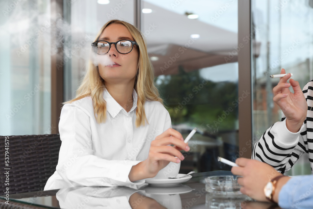 Women smoking cigarette at table in outdoor cafe Women smoking cigarette at table in outdoor cafe