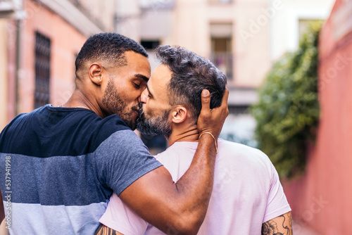 Multiracial gay couple walking and kissing on the street photo