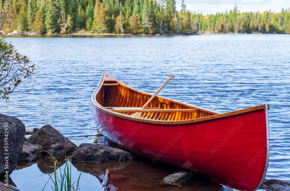 Red wooden canoe on the shore of a Boundary Waters lake on a bright autumn day