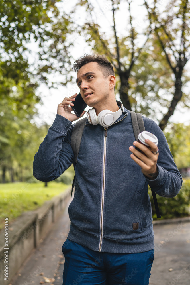 One young adult caucasian man walking in the city town near park using mobile phone smartphone talk with cup of coffee in autumn or spring day happy male tourist standing alone real people copy space One young adult caucasian man walking in the city town near park using mobile phone smartphone talk with cup of coffee in autumn or spring day happy male tourist standing alone real people copy space