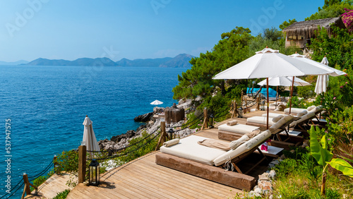 Fototapeta Naklejka Na Ścianę i Meble -  beach chairs with white umbrellas looking out over the ocean in Turkey on a summer day, beach beds on rocks looking out over the ocean