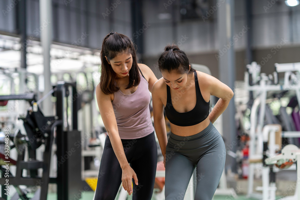 Female fitness instructor showing exercise progress to a young athletic woman at the gym and smiling cheerfully while exercising with his fitness coach and training. Female fitness instructor showing exercise progress to a young athletic woman at the gym and smiling cheerfully while exercising with his fitness coach and training.