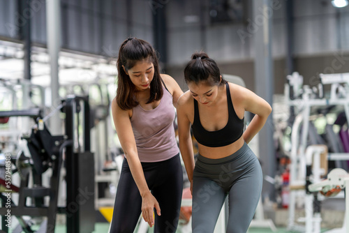 Female fitness instructor showing exercise progress to a young athletic woman at the gym and smiling cheerfully while exercising with his fitness coach and training.