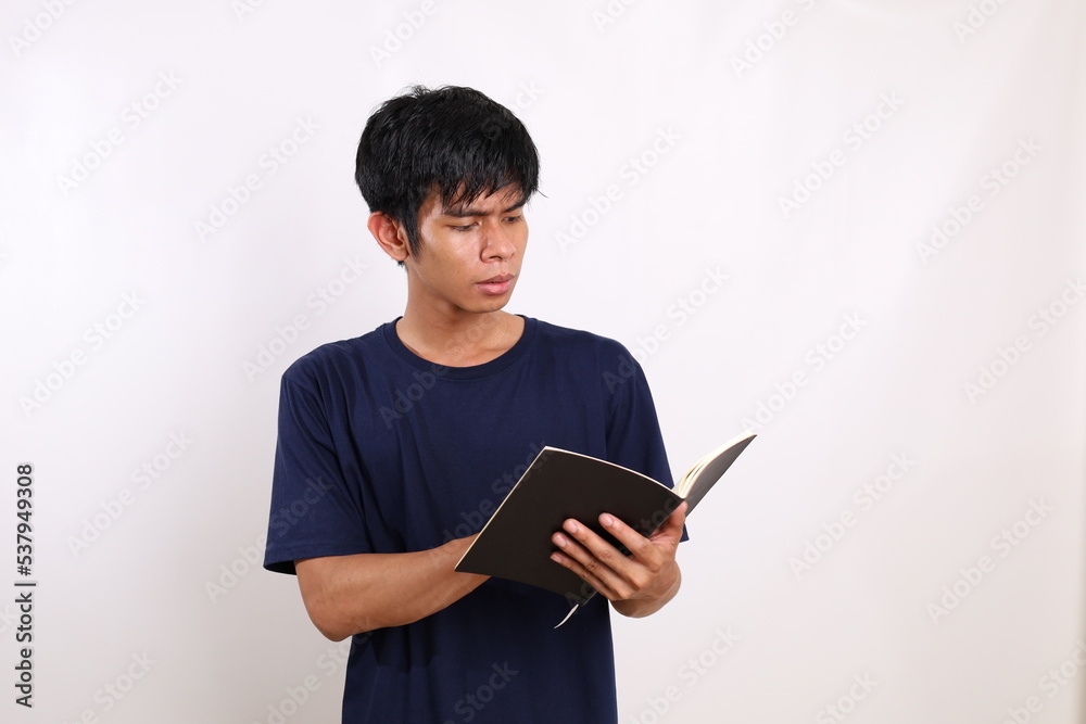 Portrait of young asian man in casual with serious face while reading a book. Isolated on white with copyspace Portrait of young asian man in casual with serious face while reading a book. Isolated on white with copyspace