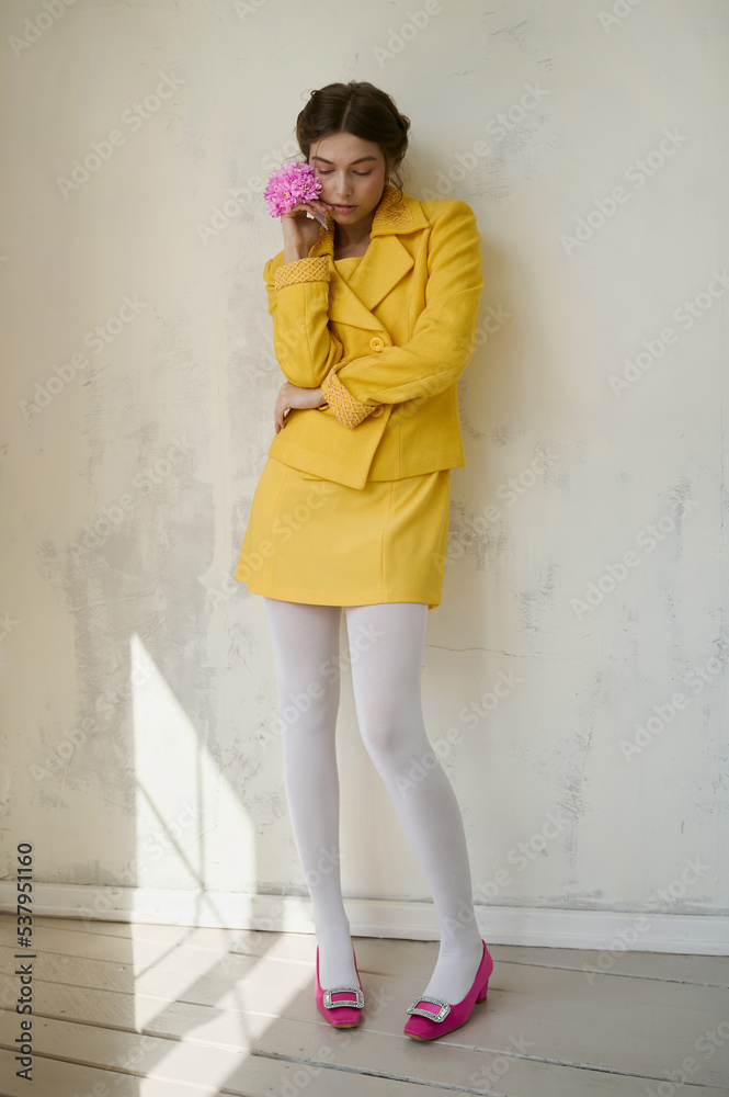 Young girl in a yellow suit with a pink flower near a white wall. Young girl in a yellow suit with a pink flower near a white wall.