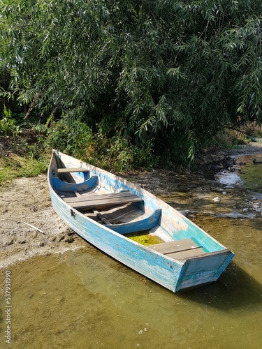 An old blue boat stands on the shore of the lake.